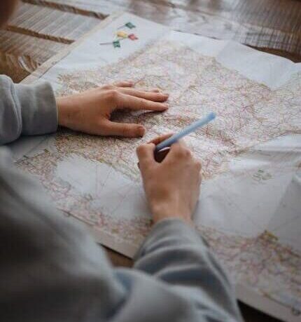 Individual marking destinations on a map with a pen while drinking water indoors.