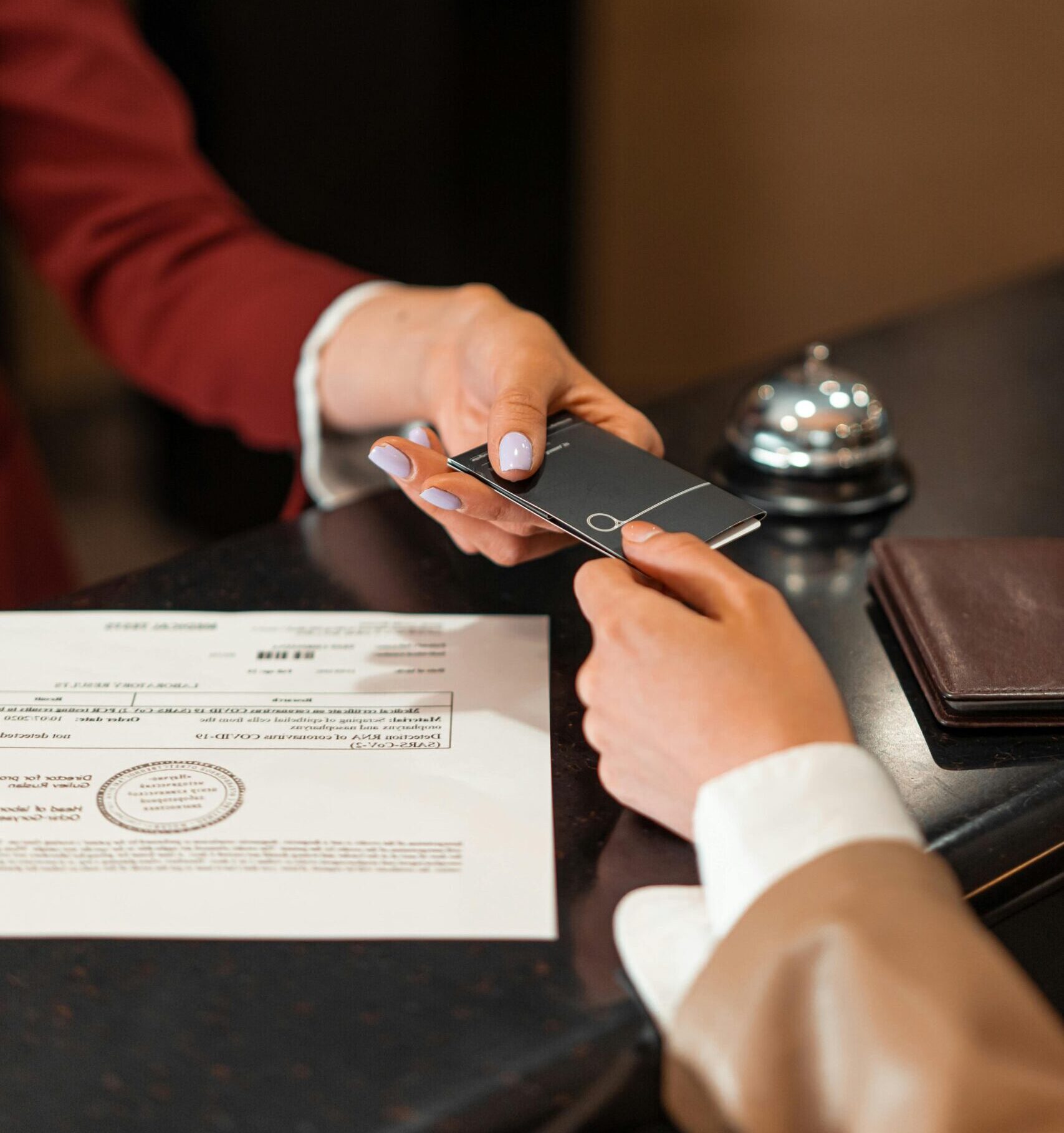 A hotel receptionist hands a key card to a guest over the counter, with documents visible.