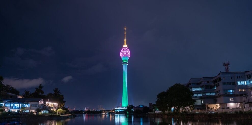 Stunning view of the illuminated Lotus Tower reflecting in the water at night in Colombo, Sri Lanka.