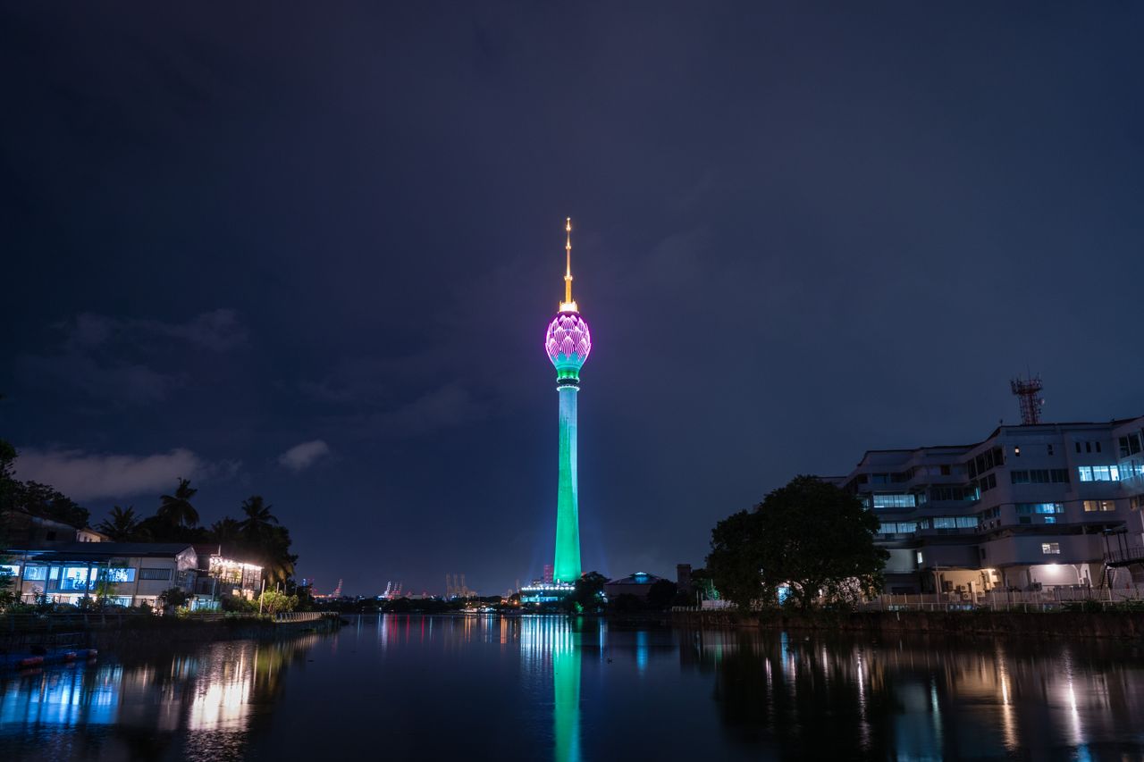 Stunning view of the illuminated Lotus Tower reflecting in the water at night in Colombo, Sri Lanka.
